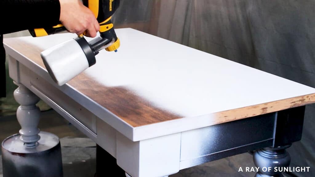 spraying coat of chalk paint on a coffee table with a paint sprayer