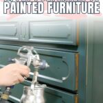 Hand using a spray gun to apply polycrylic to painted green dresser
