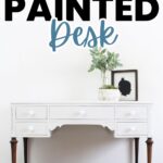 White desk with dark legs, decorated with a plant and framed art, under large CHALK PAINTED Desk text.