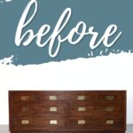 A wooden dresser with brass handles sits below a wall painted with the word before in cursive.