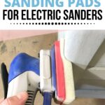 Hand holding an electric sander with a foam sanding pad, sanding a painted wooden surface.