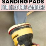 A hand holding a yellow electric sander with a foam sanding pad smoothing a painted furniture leg.