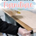 A person wearing gloves stains a wooden furniture piece. Text above reads Restaining Furniture.
