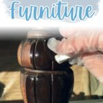 Gloved hand applying stain to dark wooden furniture leg, text above reads Restaining Furniture.