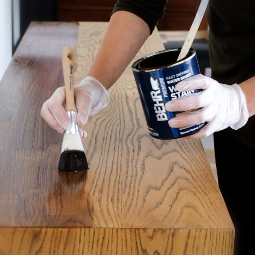 using a brush to apply wood stain onto furniture