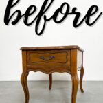 A vintage wooden side table sits in front of a wall with before written in large script.