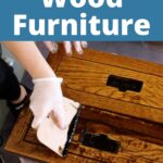 Gloved hands applying stain to wooden furniture with a sponge
