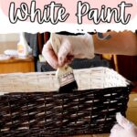 A gloved hand brushes dark gel stain over a white painted wicker basket on a table.