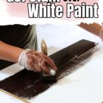 A person applies dark gel stain over white paint on a wooden board with a brush, wearing gloves.