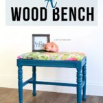 Blue painted wood bench with floral cushion under sign that reads Painting a Wood Bench.