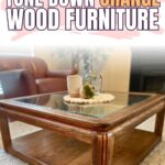 Glass-topped orange wood coffee table with decor in a cozy living room, text reads “How to Tone Down Orange Wood Furniture.”.
