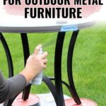 Person spray painting the black legs of an outdoor metal table placed on pink stands on grass.