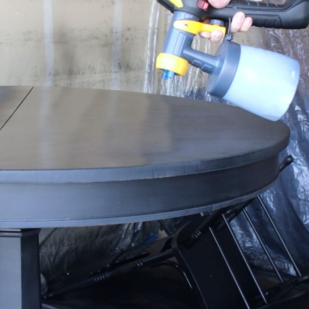 spraying black paint onto a table with a paint sprayer