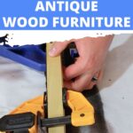 A person uses clamps to repair a crack in a piece of antique wood furniture.