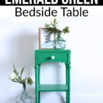 Bright emerald green bedside table decorated with glass vases and flowers, against a plain white wall.