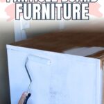 A hand rolls white paint onto a particle board cabinet