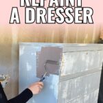 A person uses a paint roller to repaint a distressed dresser with dark brown paint.