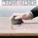 Gloved hand applying liquid to wood surface with text: How to change wood color without sanding.