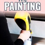 Person using a yellow paint sprayer to prime a piece of wood for painting