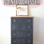 A navy blue painted dresser with four drawers, wood top, and a framed decor sign on top.