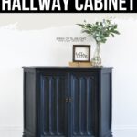 Navy blue hallway cabinet with decor on top, including a vase with greenery and a framed hello sign.