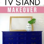 A royal blue dresser with brass handles, a large mirror, and a white vase with green leaves on top.
