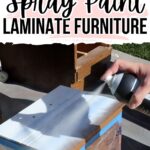 A hand spray paints a piece of laminate furniture outdoors