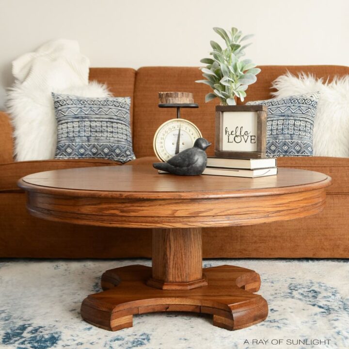 Round wooden coffee table with decor, in front of a brown sofa with blue pillows and white fur cushions.