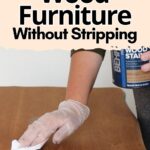 A gloved hand refinishing wood furniture with a cloth, next to a can of wood stain.