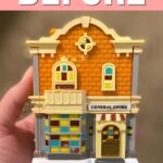 A hand holds a small model of an orange brick general store