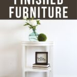 White painted mahogany end table with vase, flowers, books, and decor against a white wall