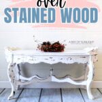 Distressed White Painted Ornate table sits against a wall; text above reads “Painting over stained wood.”.