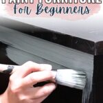 Hand painting a dark wooden dresser with white paint, with the text How to Paint Furniture for Beginners.