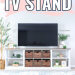 White DIY TV stand with baskets, plants, and decor, holding a large flat-screen TV against a light wall.