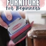 A hand uses an electric sander on wooden furniture with the text Sanding Furniture For Beginners.
