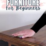 A hand sanding a wooden piece of furniture; text reads Sanding Furniture For Beginners.