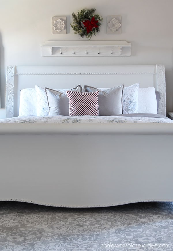 White bed with multiple pillows, a festive wreath above headboard