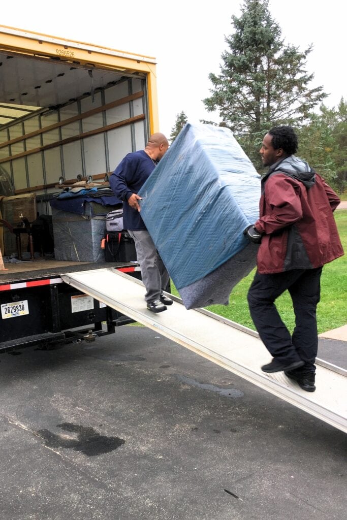 two people carrying blanket wrapped dresser into truck for shipping