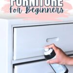 Hand spray painting a white dresser with text: How to Spray Paint Furniture for Beginners.
