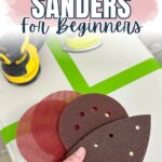 A hand holds various sanding pads near electric sanders on a table labeled Best Sanders for Beginners.