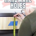Person measuring drawer front with tape measure and pencil, preparing to drill new hardware holes.