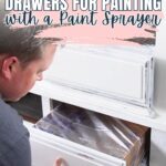 A person tapes off a drawer with plastic for painting, prepping it inside a white dresser.