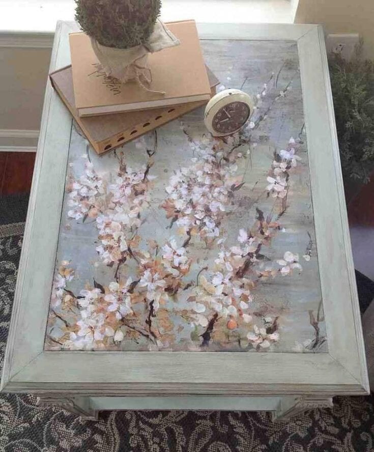 Table with floral art, and a plant, two books, and a clock placed on it