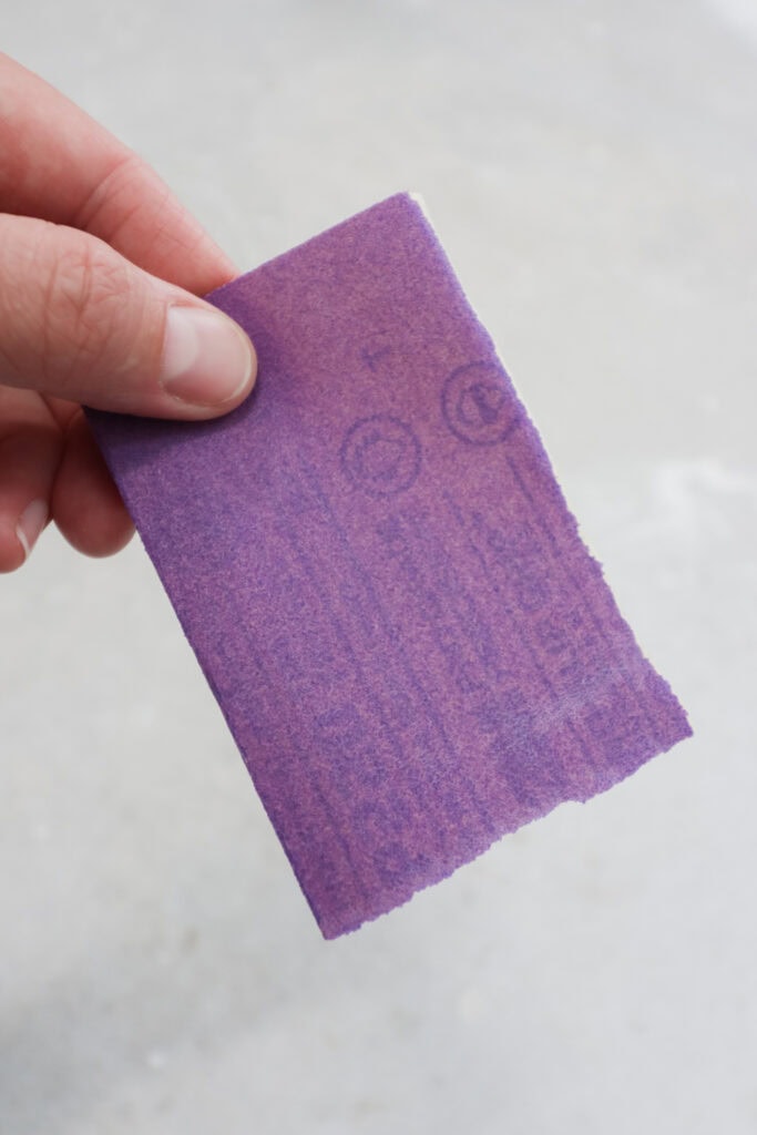 A hand holding purple sandpaper