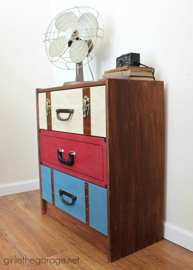 Wood dresser with multicolored drawers, a vintage fan, and books placed on top, against a white wall.