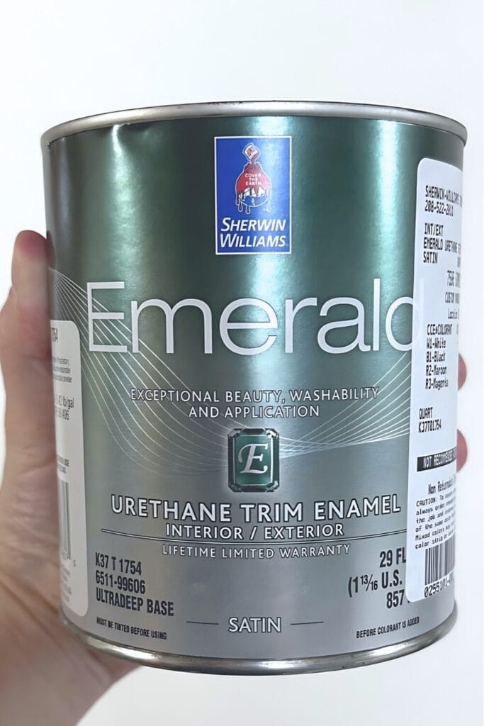 A hand holds a can of Sherwin-Williams Emerald Urethane Trim Enamel paint in satin finish.