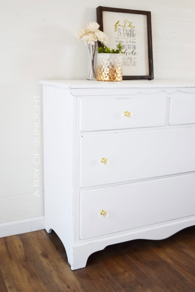 Side view of dresser with gold knobs, decorated with flowers and a framed quote on top.