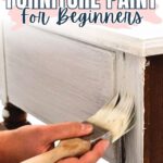 A hand painting white paint on wooden furniture with text: Best Types of Furniture Paint for Beginners.