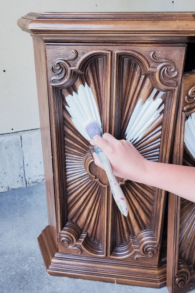 Hand using brush to paint on wood furniture with details