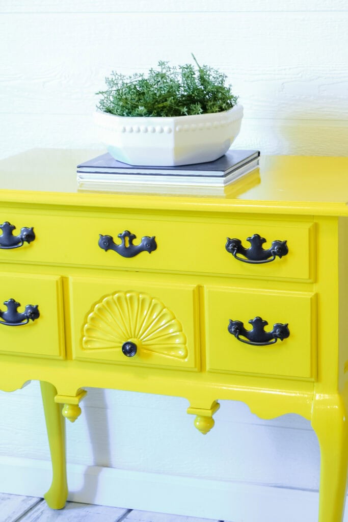 Bright yellow vintage side table, topped with books and a white bowl of greenery.